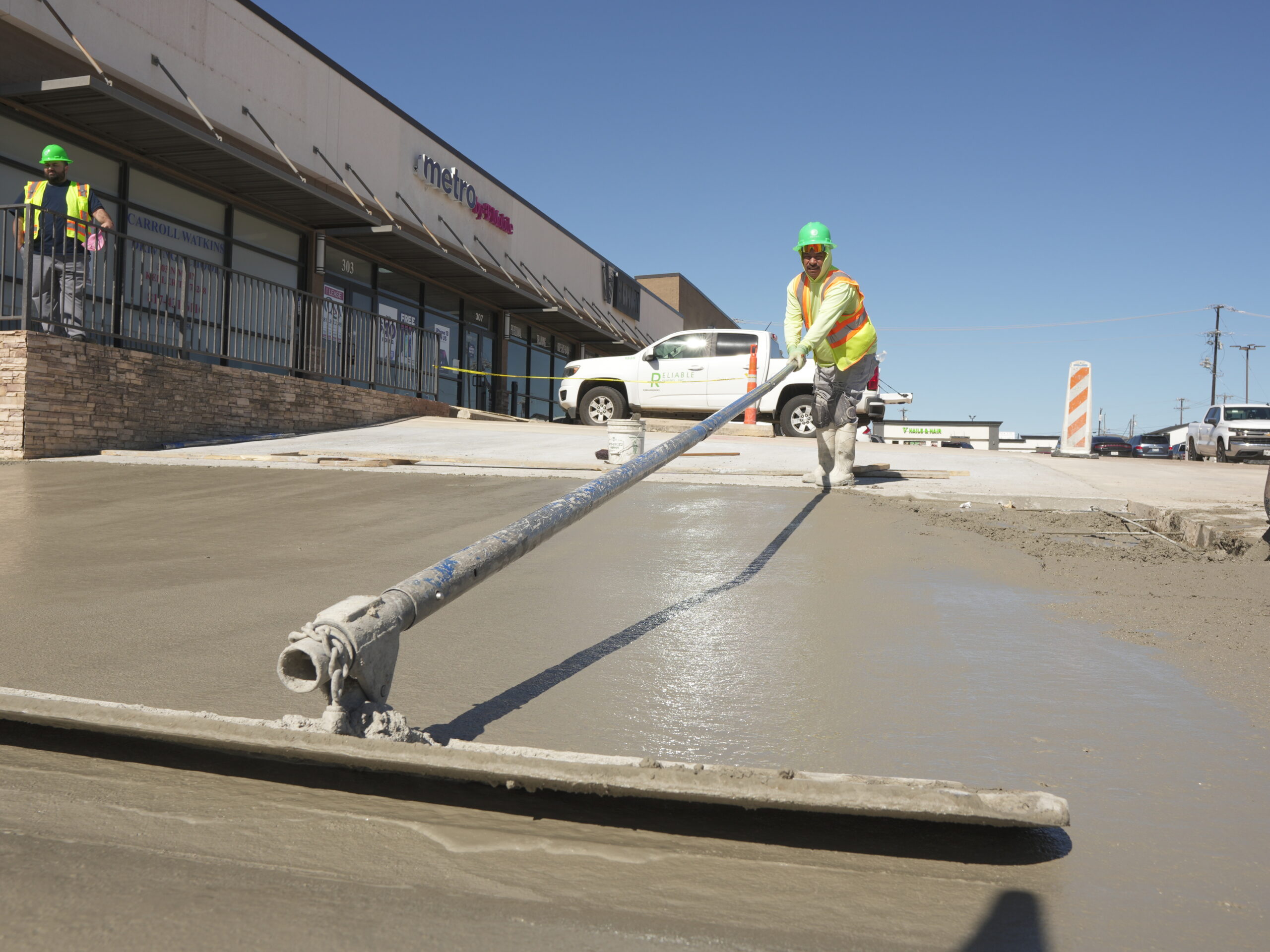 Reliable Paving crew pouring and hand-finishing a concrete parking lot outside a North Texas retail center